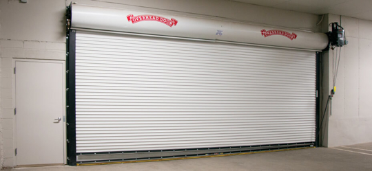 A horizontal rolling garage door with white slats is mounted in a concrete wall.
