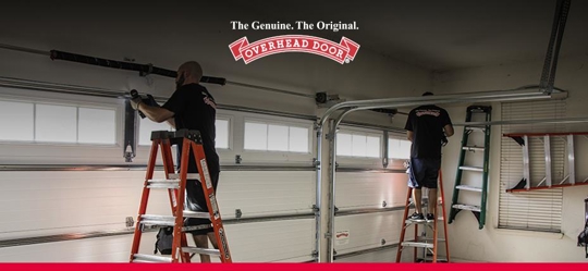 Two Overhead Door technicians repair a garage door.